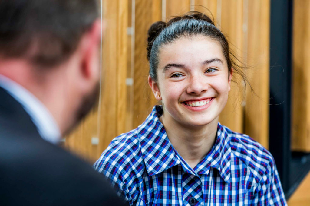 A female student smiles while speaking to a teacher