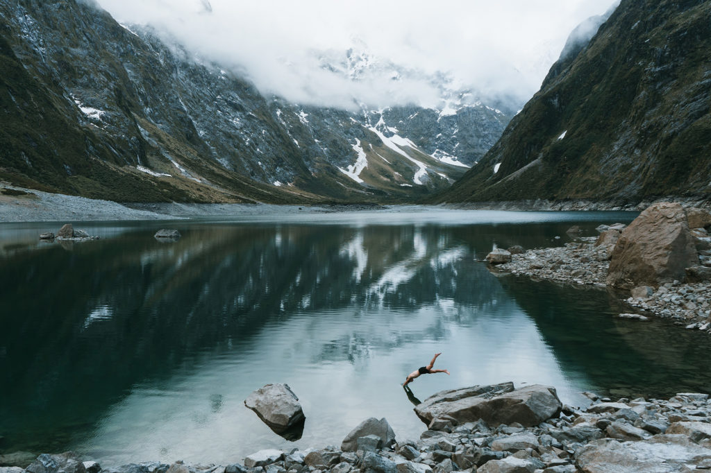 A man dives into a lake, with mountains being seen in the background