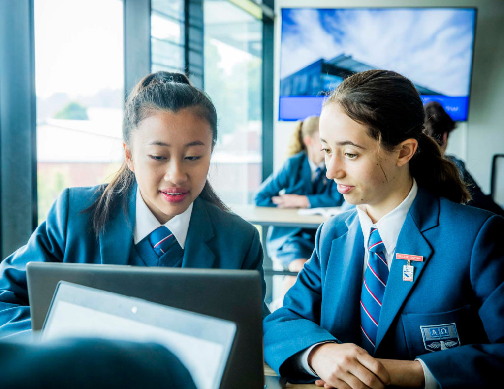 Two female students chat while using a laptop